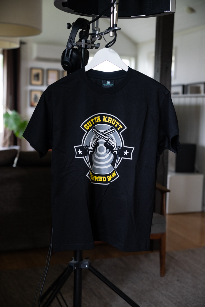 Svart t-skjorte med “Gutta Krutt”-motiv i offwhite, støvet gul, kullgrå og militærgrå toner.