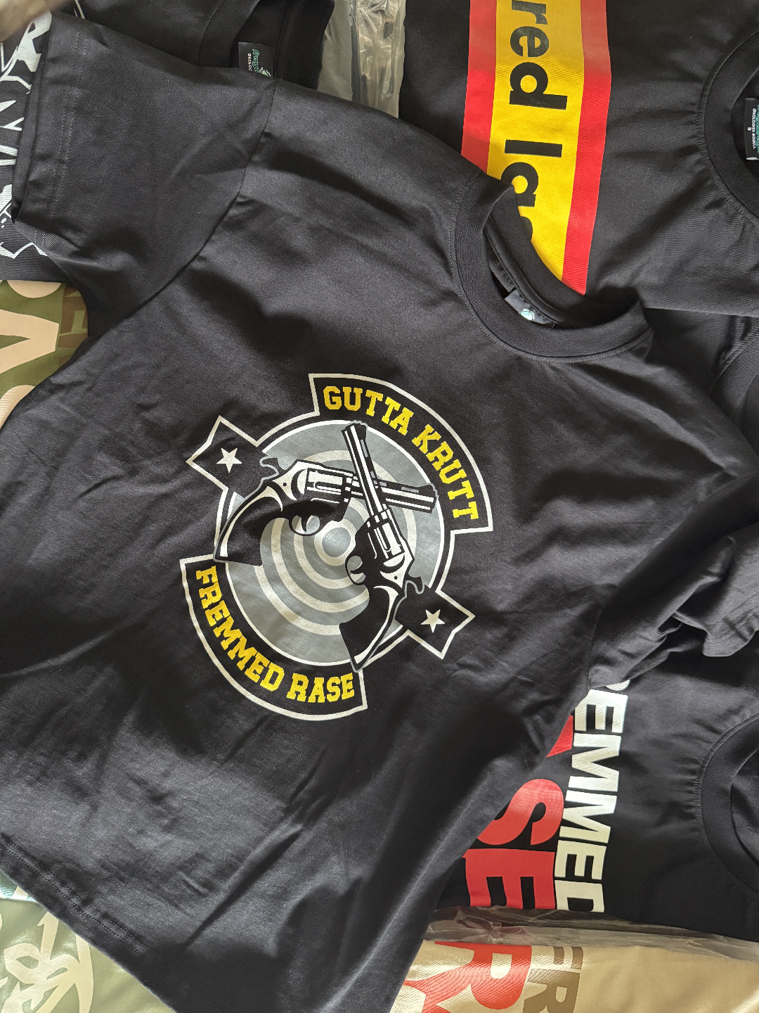 Svart t-skjorte med “Gutta Krutt”-motiv i offwhite, støvet gul, kullgrå og militærgrå toner.